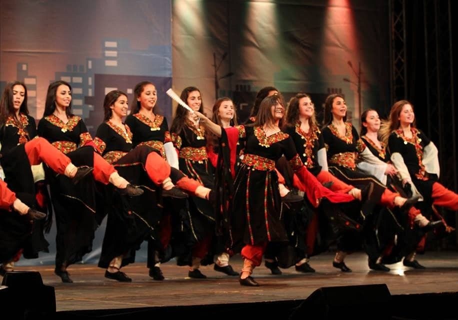 A line of dancers performing dabke, holding hands and kicking in unison